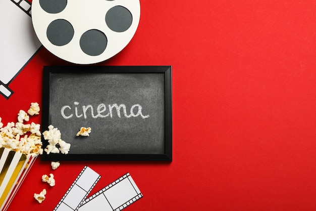 Blackboard with text paper cup with popcorn film and reel on red background space for text