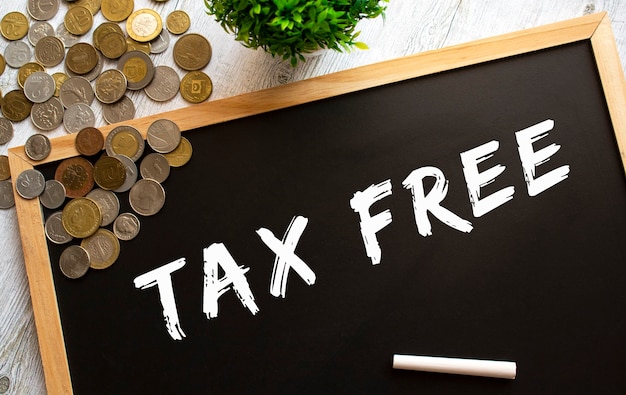 Blackboard with the text TAX FREE and metal coins on a gray wooden table.