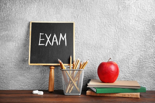 Blackboard with word EXAM notebooks and apple on table