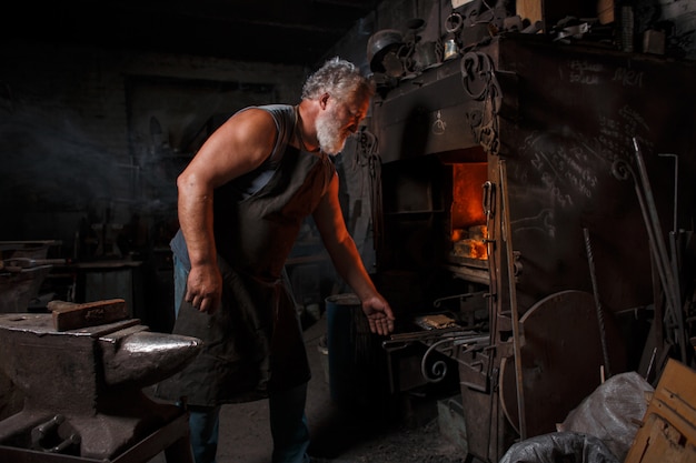 Blacksmith craftsman in apron works in blacksmith's shop