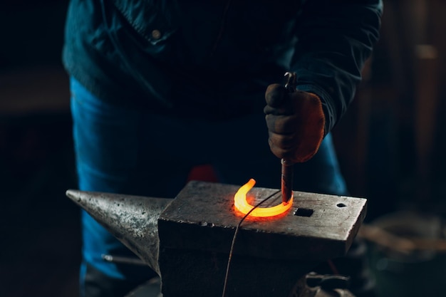 Blacksmith forges and makes metal detail with hammer and anvil at forge