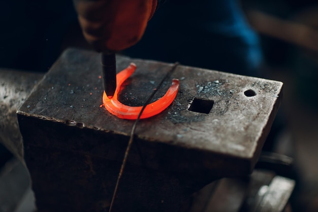 Blacksmith forges and makes metal detail with hammer and anvil at forge