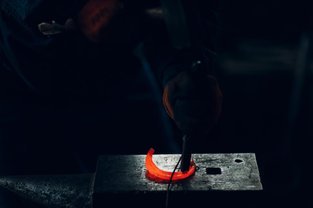 Blacksmith forges and makes metal detail with hammer and anvil at forge