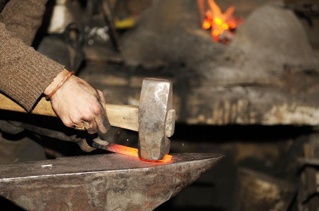 Photo blacksmith working metal with hammer on the anvil in the forge