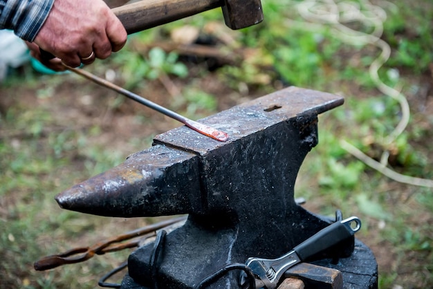 blacksmith works on an anvil. Master forges product. Tools and blacksmith anvil. Blacksmith working outdoors.