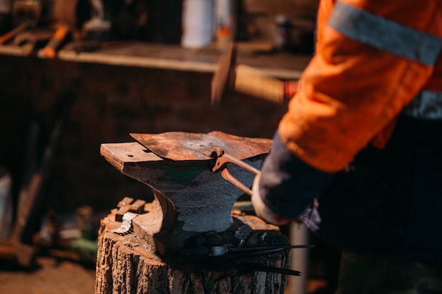 Blacksmith workshop. The blacksmith works on the anvil with a hot metal billet.