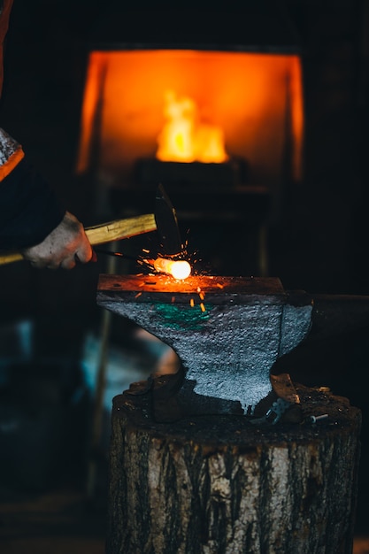 Blacksmith workshop. The blacksmith works on the anvil with a hot metal billet.