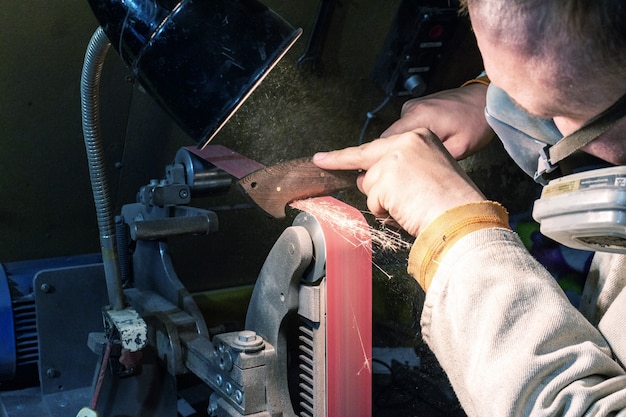 Blade sharpening creating on a belt grinder process. Knife making master hands close up.