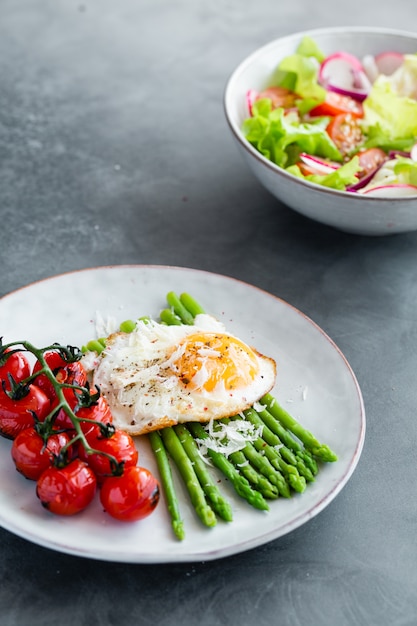 Blanched asparagus, fried egg, tomatoes and sald on the bowl. 