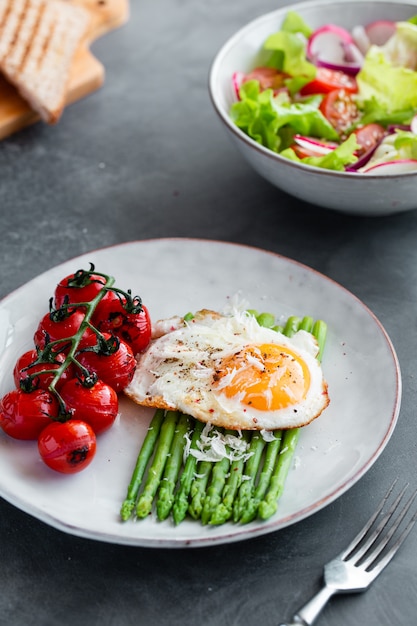 Blanched asparagus, fried egg, tomatoes and sald on the bowl.