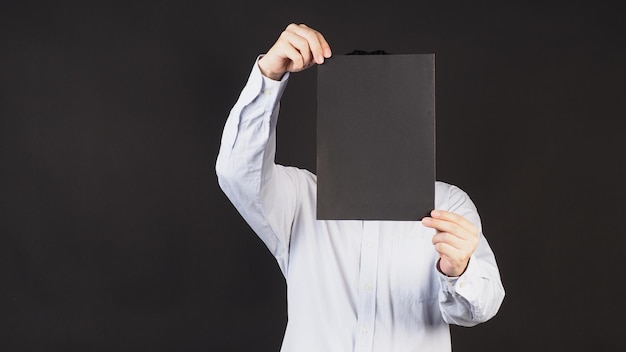 Blank black board A4 paper in man hand covered face and wear blue shirt on black background