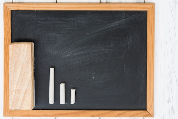 Blank black board,white chalk and eraser on grunge wooden background,top view