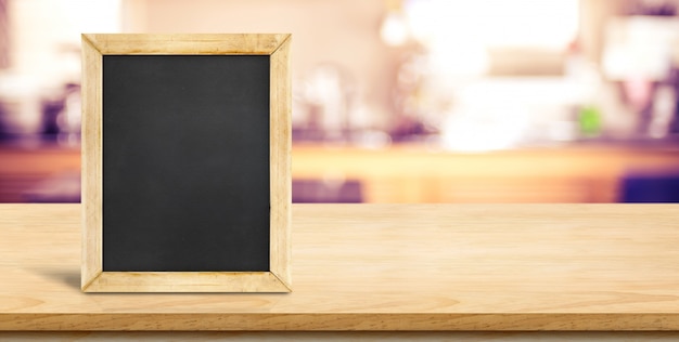 Blank blackbaord on plank wooden table top with blurred home kitchen