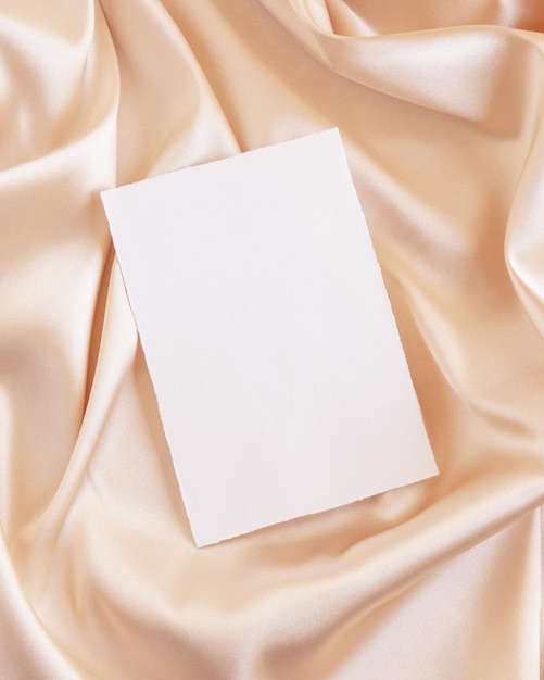 Blank card on beige silky fabric drapery top view greeting or wedding mockup