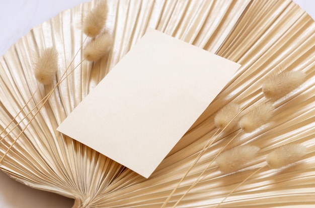 Blank card on dry beige palm leaf near hare's tail grass close up boho wedding mockup