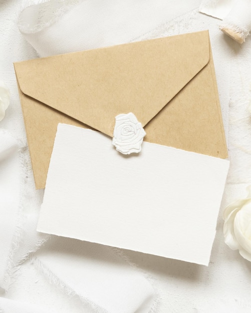 Blank card and envelope near cream roses and white silk ribbons top view wedding mockup