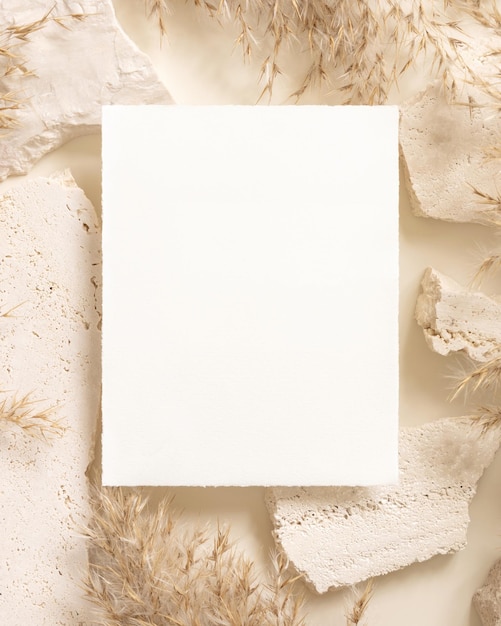 Blank card near beige travertine stones and dried pampas grass top view greeting mockup