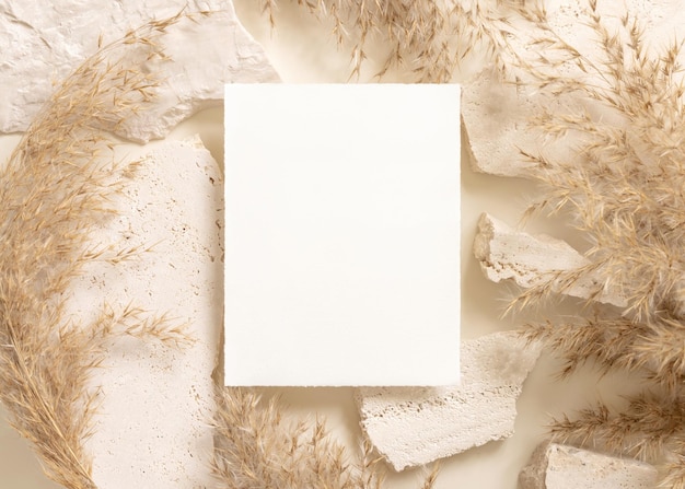 Blank card near beige travertine stones and dried pampas grass top view greeting mockup