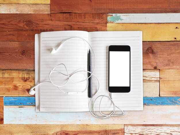 Blank cell phone notebook and headphones on a wooden background