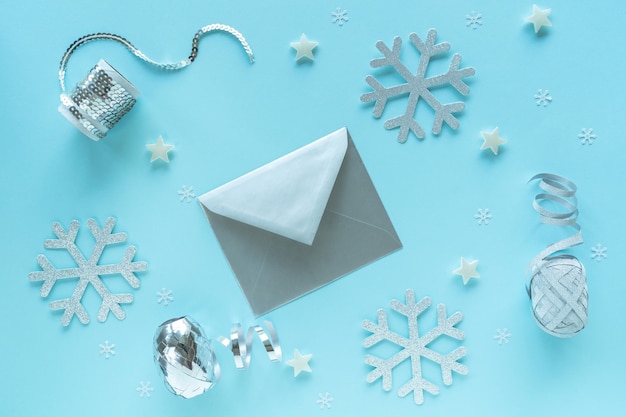 Blank christmas card and envelope with silver decorations on blue surface, top view. Holiday hipster