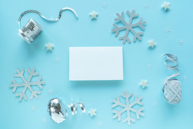 Blank christmas card with christmas silver decorations on blue surface, top view. Holiday hipster