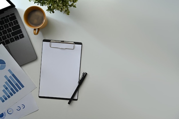 Blank clipboard laptop computer coffee cup and financial reports on white office