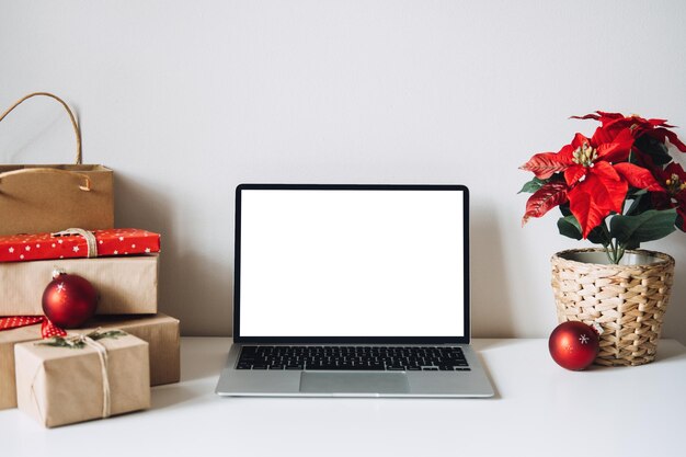 Blank display screen laptop computer with poinsettias christmas flower and gift boxes on white table