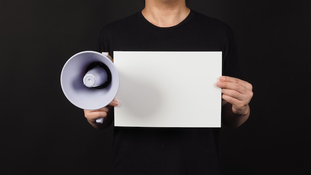 Photo blank empty paper in man's hand with megaphone on black background.