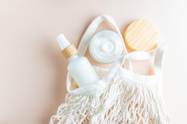 Blank frosted glass spray bottle and bamboo jar on beige background with cotton mesh bag Organic spa cosmetic beauty product mock up Zero waste concept