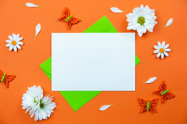 Blank greeting card mockup on colorful orange surface with white daisy flowers and butterflies decoration