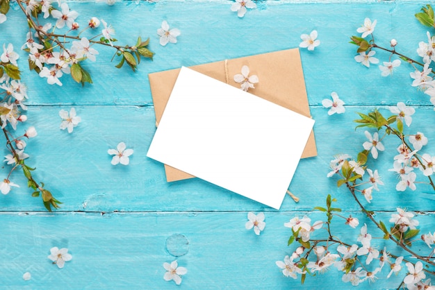 Blank greeting card with spring cherry flowers on blue wooden table. flat lay. top view