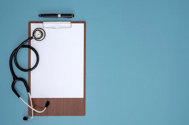 Blank medical clipboard, stethoscope and pen on light blue background with copy space.