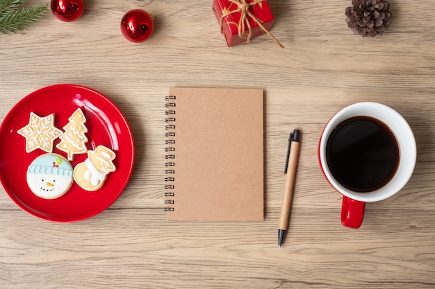 Blank notebook, black coffee cup, Christmas cookies and pen on wood table, Top view and copy space. Xmas, Happy New Year, Goals, Resolution, To do list, Strategy and Plan concept