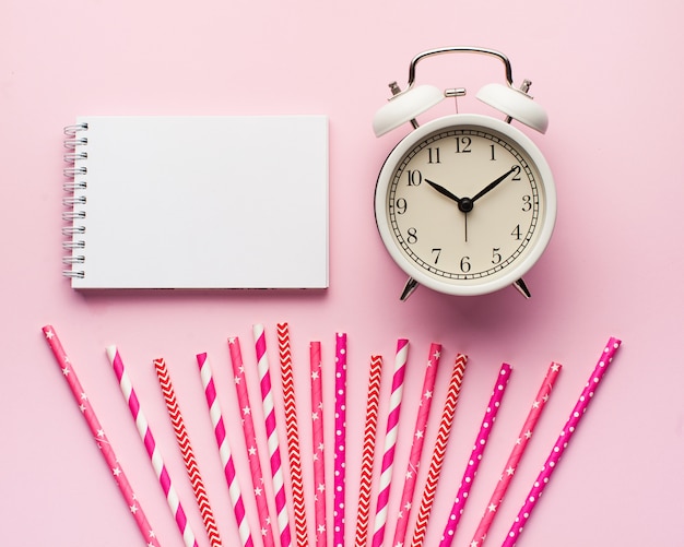 Blank notebook, clock, pink paper tubes for cocktails.