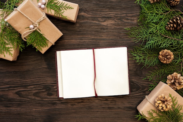 Blank notebook, gifts boxes, branch and fir cones on wooden. top view