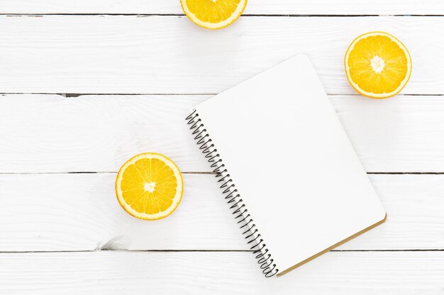 Blank notebook and halves of oranges on a white wooden background flat lay