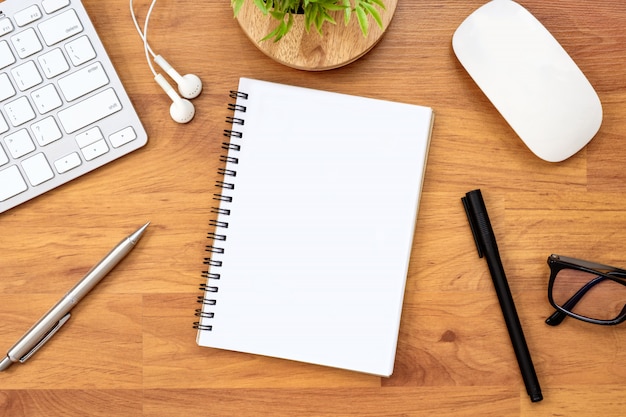 Blank notebook is on top of wood office desk table with supplies. Top view, flat lay.