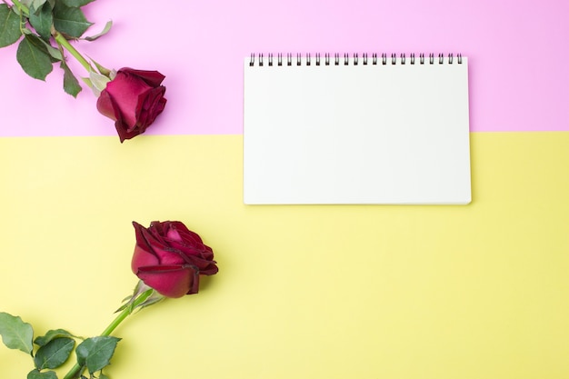 Blank notebook on pink and yellow paper with roses, flat lay, top view.