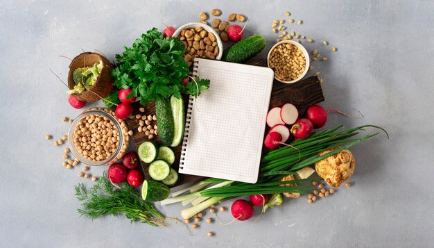 Blank notebook with fresh vegetables, herbs, legumes and nuts top view. Veggie Cooking Concept