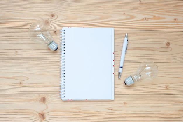 Blank notebook with lightbulb and crumbled paper on wooden table