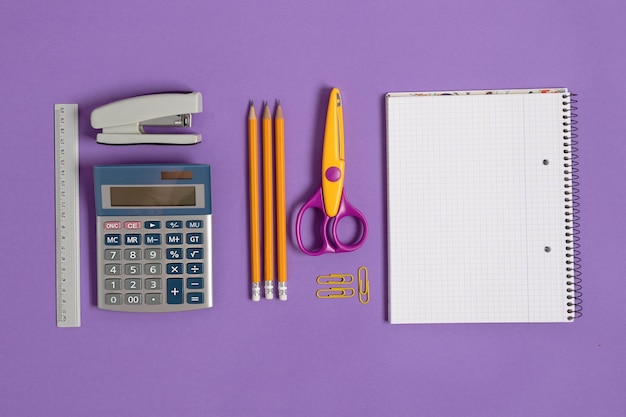 Blank notebook with school and office supplies on purple background top view