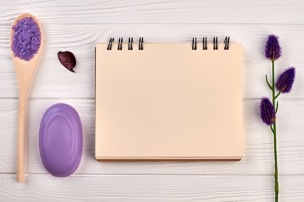 Blank notepad for copyspace and spa accessories. Purple soap with salt and lavender on white wooden desk.