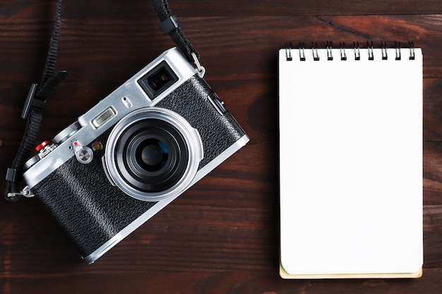 Blank notepad page and modern camera in classic style on dark brown wooden table