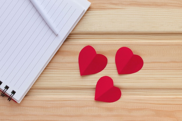 Blank notepad, pen and red hearts on wooden table. Love message. Natural surface. Valentine's Day theme. Flat lay, top view, copy space.