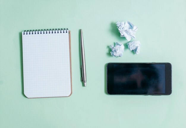 Blank notepad and phone on blue space with pen.