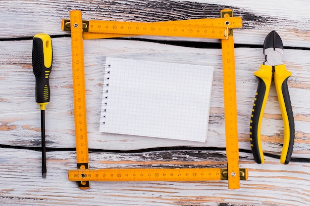 Photo blank notepad in a ruler square with repair tools. top view flat lay. white wooden background.