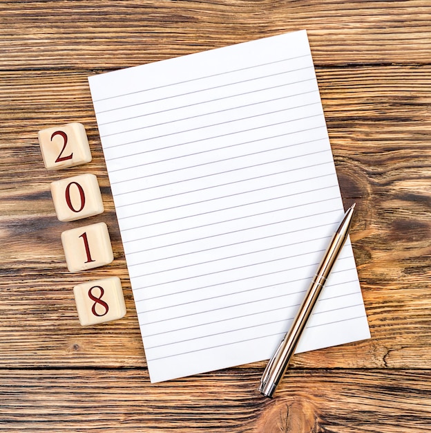 Blank notepad with pen and 2018 written by wooden cubes on the table