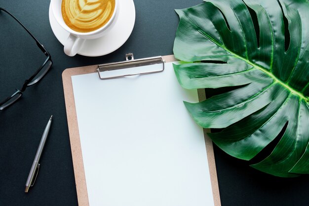 Blank notepaper with tropical leaves and accessories laying on black table.Home office,workspace design backgrounds,flat lay,top view