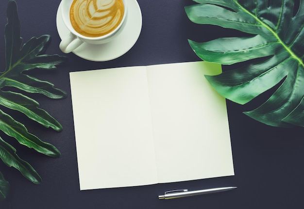 Blank notepaper with tropical leaves and accessories laying on black tableHome officeworkspace design backgroundflat laytop view