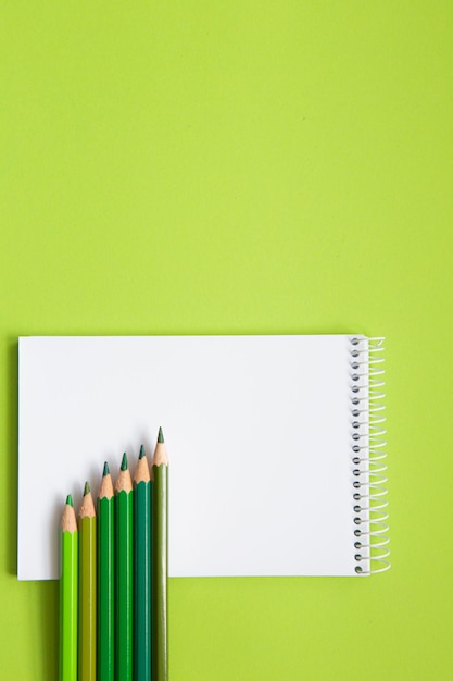 Blank page of a notebook on a green background and colored pencils